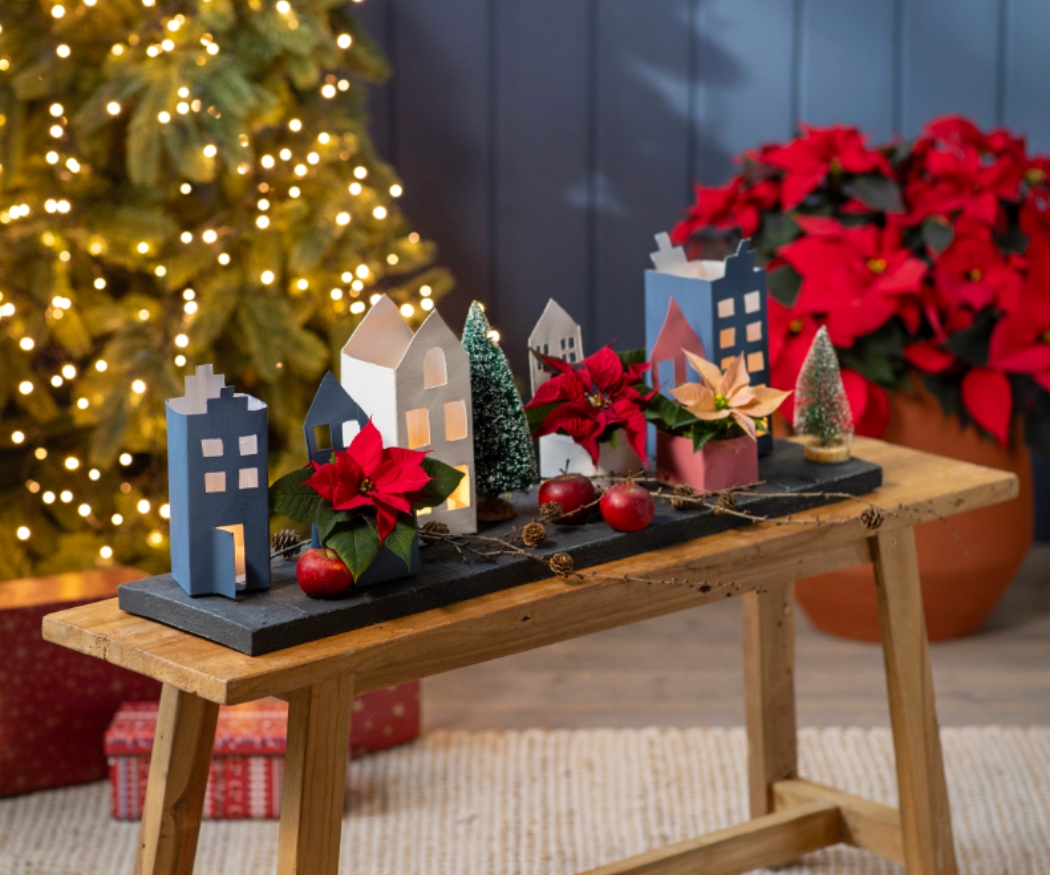 Това завършено ръчно направено зимно селце е с празнична коледна украса, включително мини поинсетии, картонени къщички, ябълки и шишарки. Идеално за празнично творчество с деца!