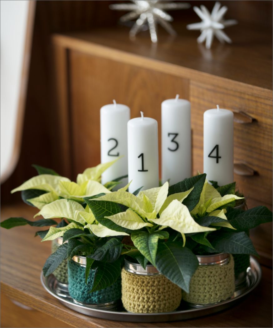 2017-weihnachtsst Silbernes Tablett auf Holzmöbel, darauf stehen umhäkelte Konservendosen mit vier cremefarbenen Mini-Weihnachtssternen und mit weißen Zahlenkerzen mit Beschriftung 1, 2, 3, 4