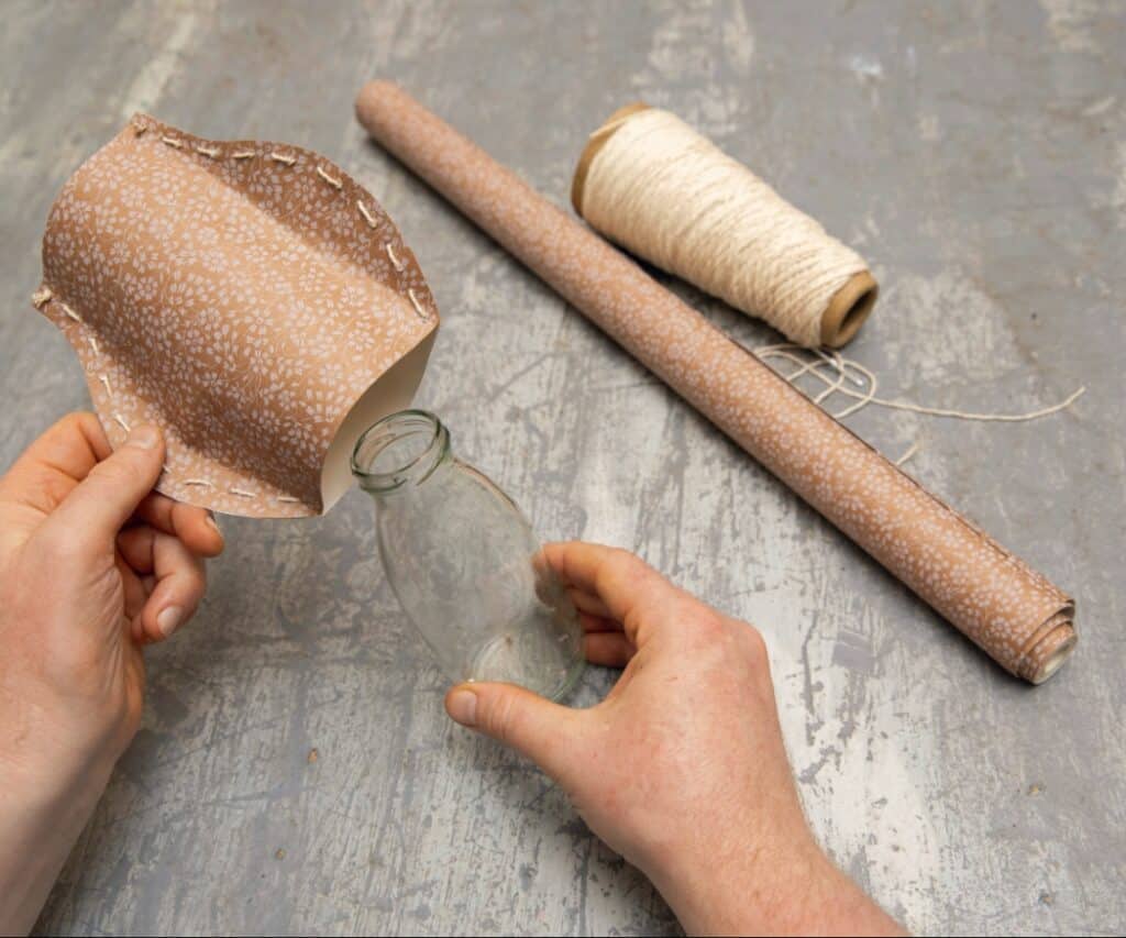 Genähtes Papierstück wird über eine Glasflasche gestülpt.
