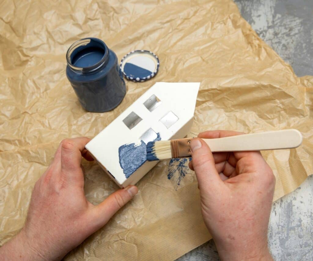 Ein Upcycling-Haus aus Karton wird mit blauer Farbe bemalt – Schritt für Schritt entsteht ein festliches Miniaturdorf.