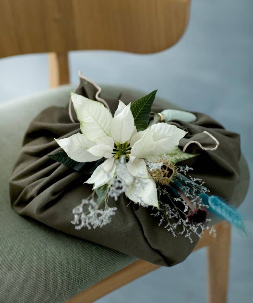 Geschenk in Tuch mit weißem Schnittweihnachtsstern, Trockenblumen und blaugrünen Gräsern