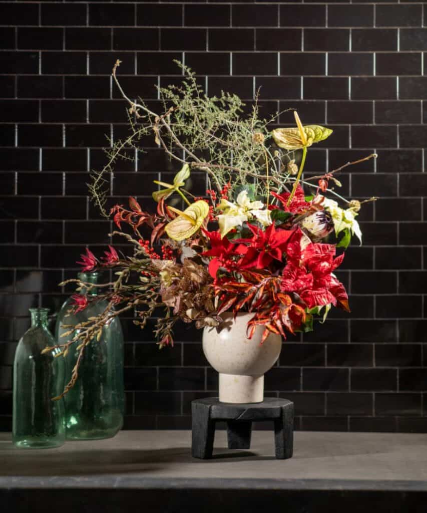 Moderner Weihnachtsstrauß mit roten Weihnachtssternen und exotischen Blüten vor dunkler Wand