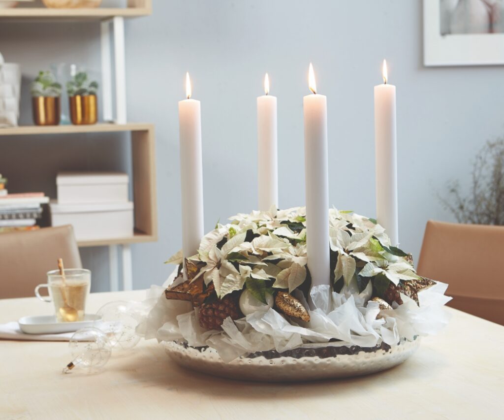 A white Advent wreath without fir, featuring baking paper, white poinsettias, pine cones and four taper candles. 