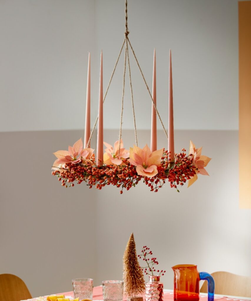 A hanging Advent wreath made from rosehip twigs, featuring apricot cut poinsettias and four slender taper candles.