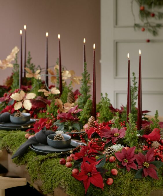 2021_poinsettia_05000_Christmas_Woodland_03-563x675 Un festivo centro de mesa de temática forestal con mini flores de Pascua y velas altas.