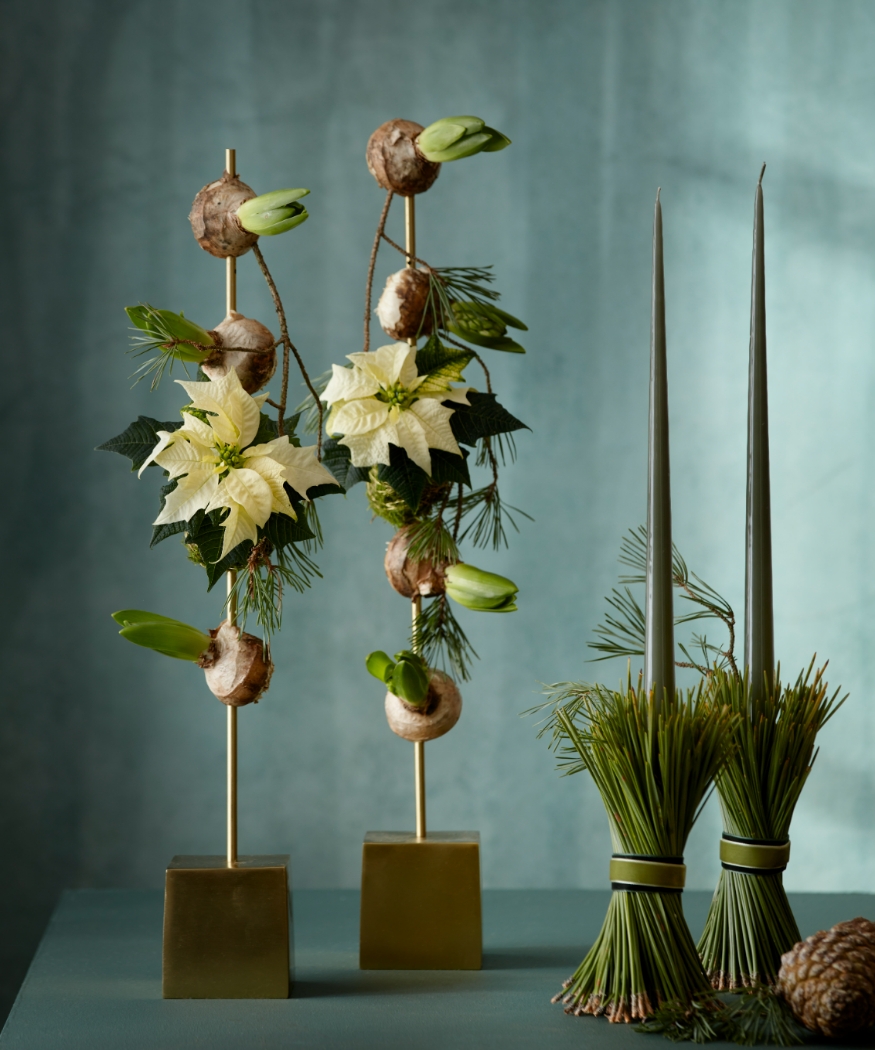 Décorations de Noël modernes composées de kokedamas de poinsettias, de bulbes d’amaryllis, de brindilles et de grandes bougies.