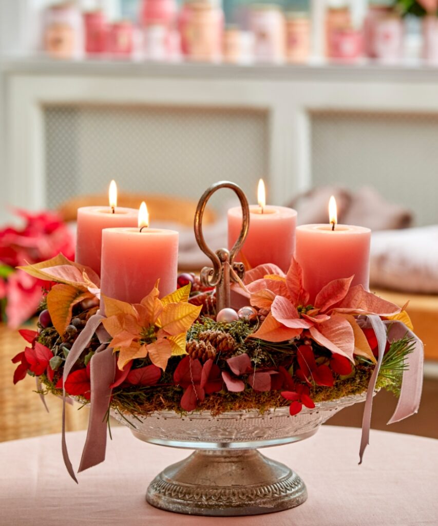 Une couronne de l'Avent réalisée à partir de branches de sapin et de mousse, agrémentée de bougies couleur rose poudré et de poinsettias coupés dans les tons rose et abricot.