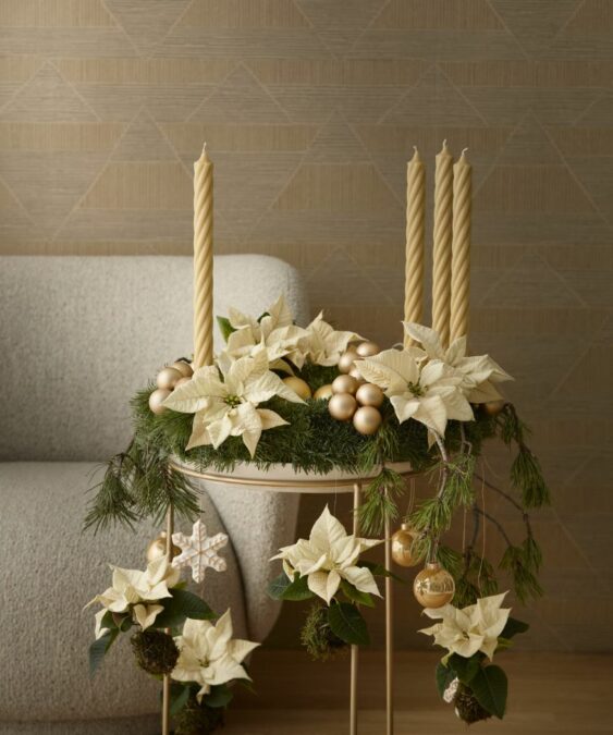 Egy prémium adventi koszorú arany árnyalatokban, krémfehér mini mikulásvirággal és harmonizáló díszítőelemekkel egy elegáns asztalon elrendezve. 