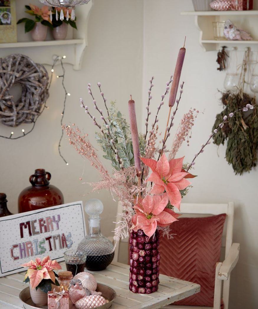 2020-weihnachtsstern-04000-weihnachtlicher-landhauscharme-25 Degli steli decorativi di Poinsettia in delicate tonalità di rosa sono integrati in un bouquet. Dei fiori secchi completano la composizione, collocata su una tavola natalizia.