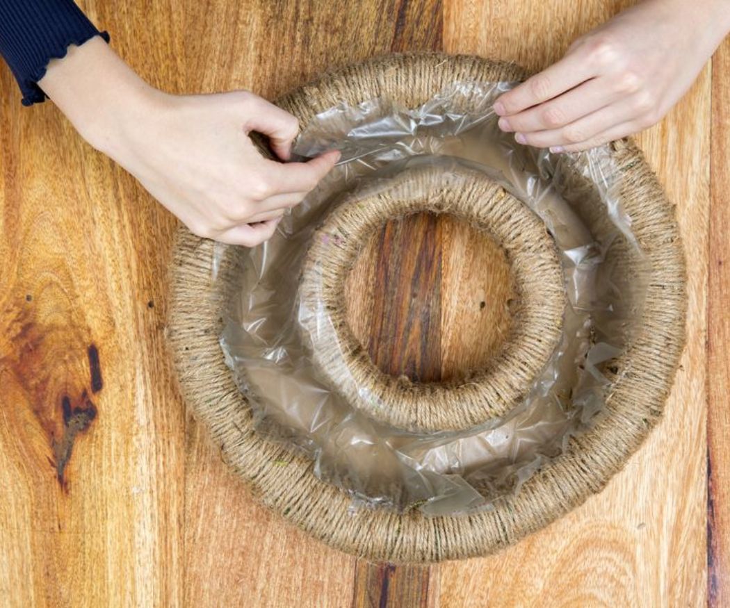 2016-weihnachtsstern-diy-dventskranz-04 Un paio di mani posizionano un telo di plastica in una fessura per una corona d'Avvento fatta in casa.