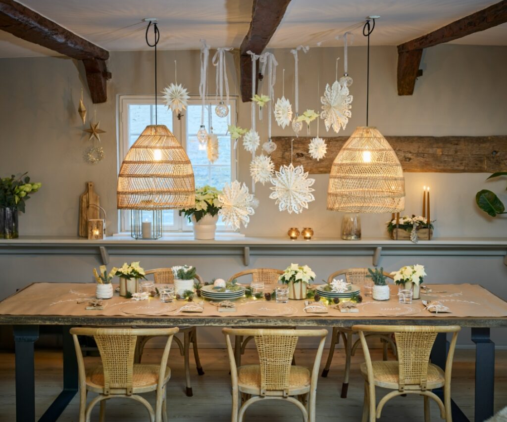 Un'accogliente tavola da pranzo è allestita con Stelle di Natale bianche, stelle di carta e decorazioni natalizie naturali in stile Scandi. 