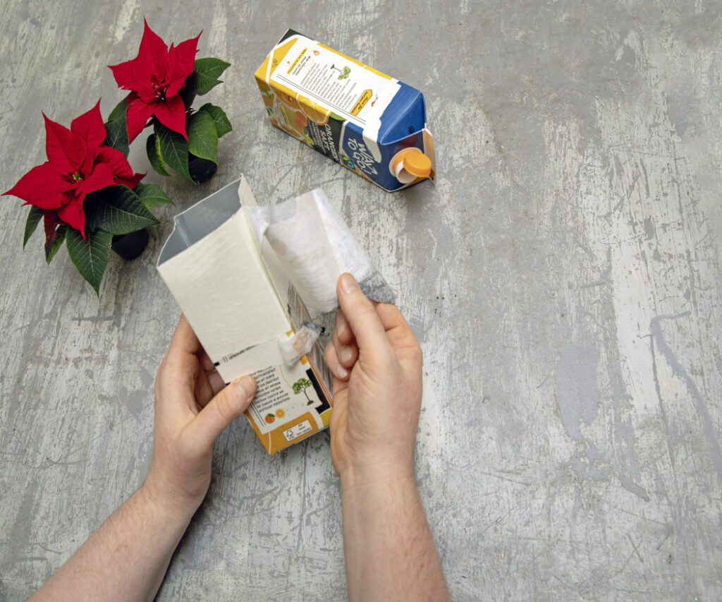 La prima fase di questo progetto creativo di riciclo natalizio da fare con i bambini: due mani rimuovono lo strato esterno di un cartone per bevande. 