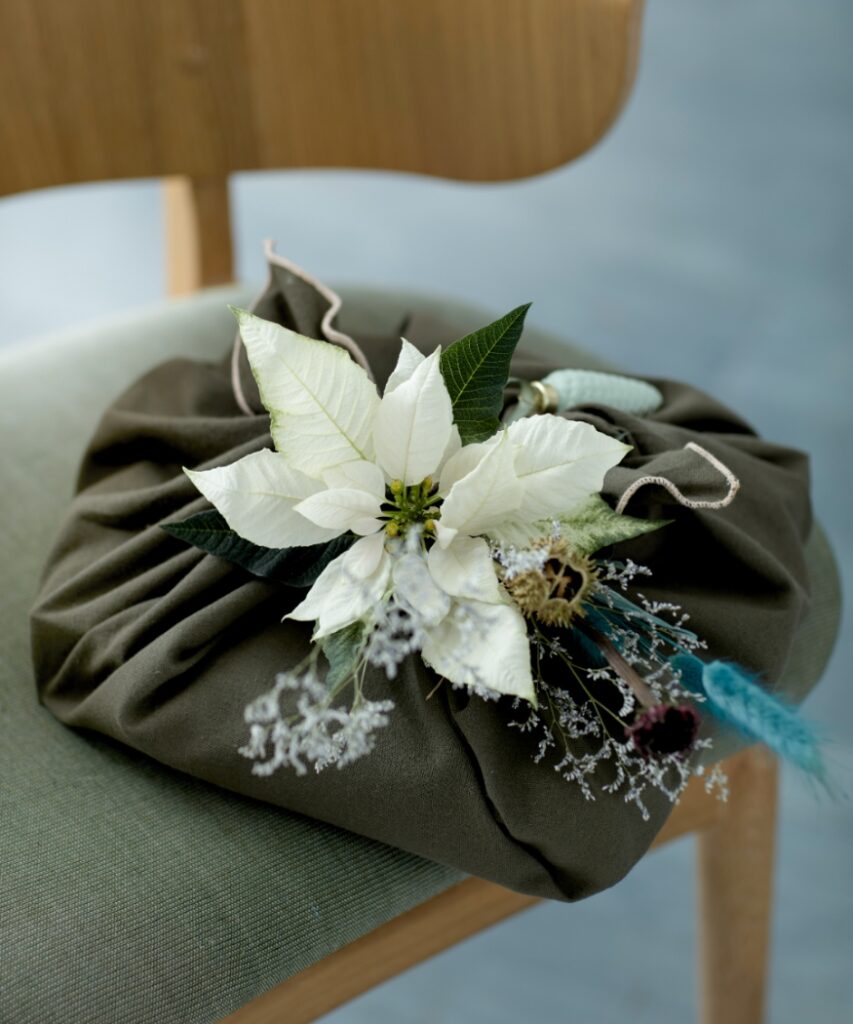 Regalo avvolto in un panno con Stella di Natale bianca recisa, fiori secchi e graminacee verde-azzurre 