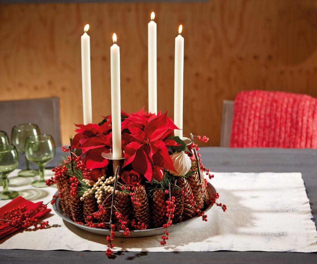 Een adventskrans van sparrenappels, mos, dennentakken en takken van winterbes (Ilex verticillata), met vier witte kaarsen en een rode kerstster in het midden.