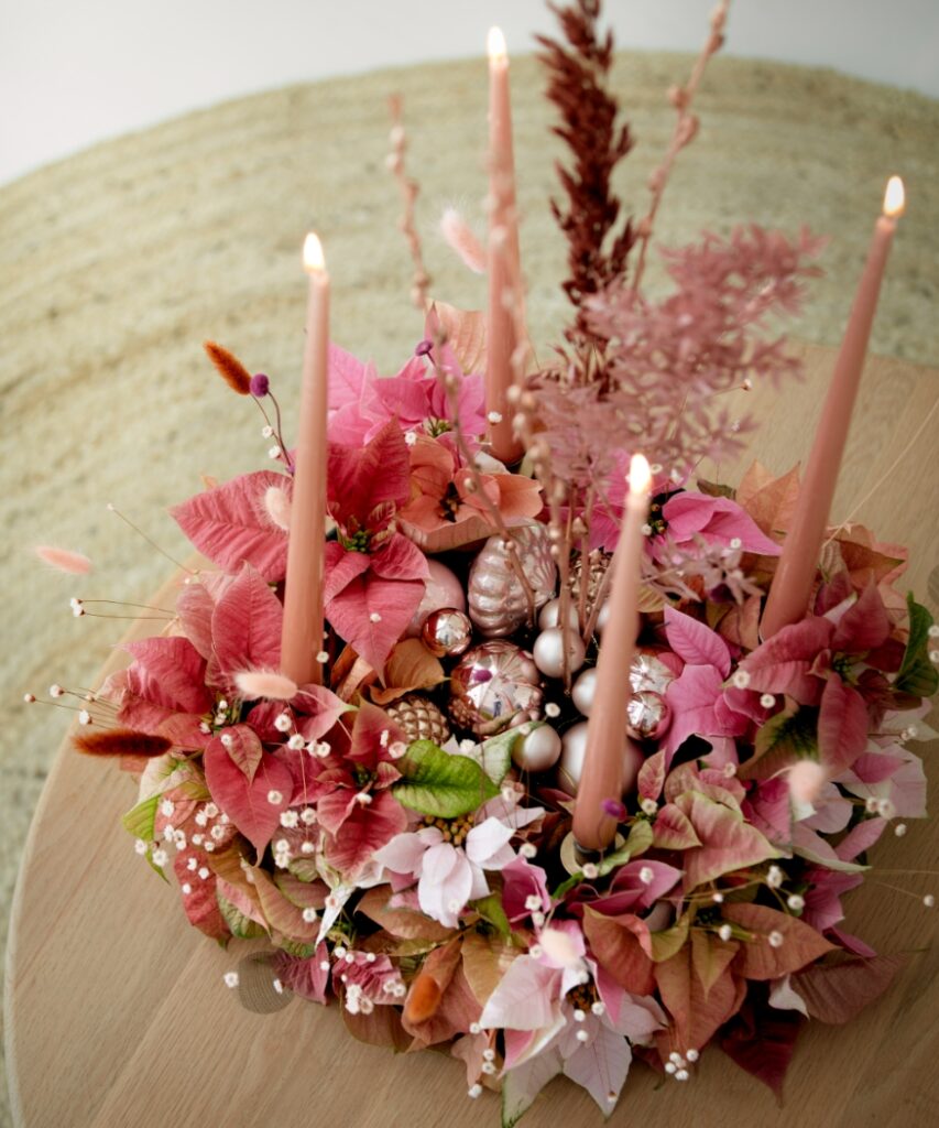 Een boho-adventskrans met kerststerren in roze en abrikoos, droogbloemen, grassen en oudroze dinerkaarsen.