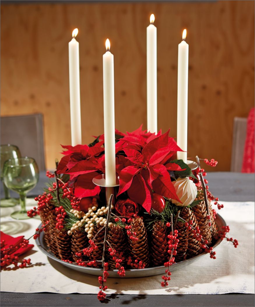 Adventskranz im Landhausstil aus Zapfen, Weihnachtssternen, roten Beeren und weißen Kerzen auf einem grauen Tisch mit weißer Leinentischdecke